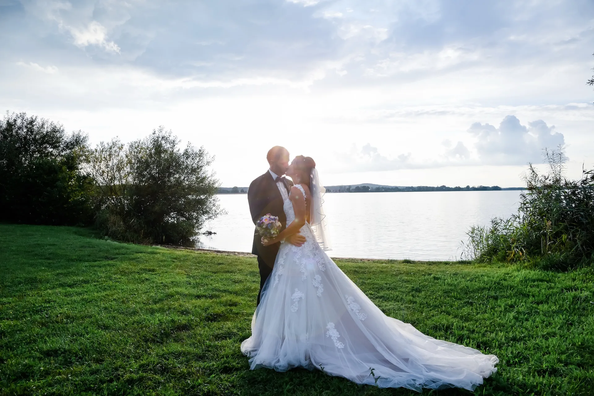 Brautpaar auf Wiese mit See im Hintergrund