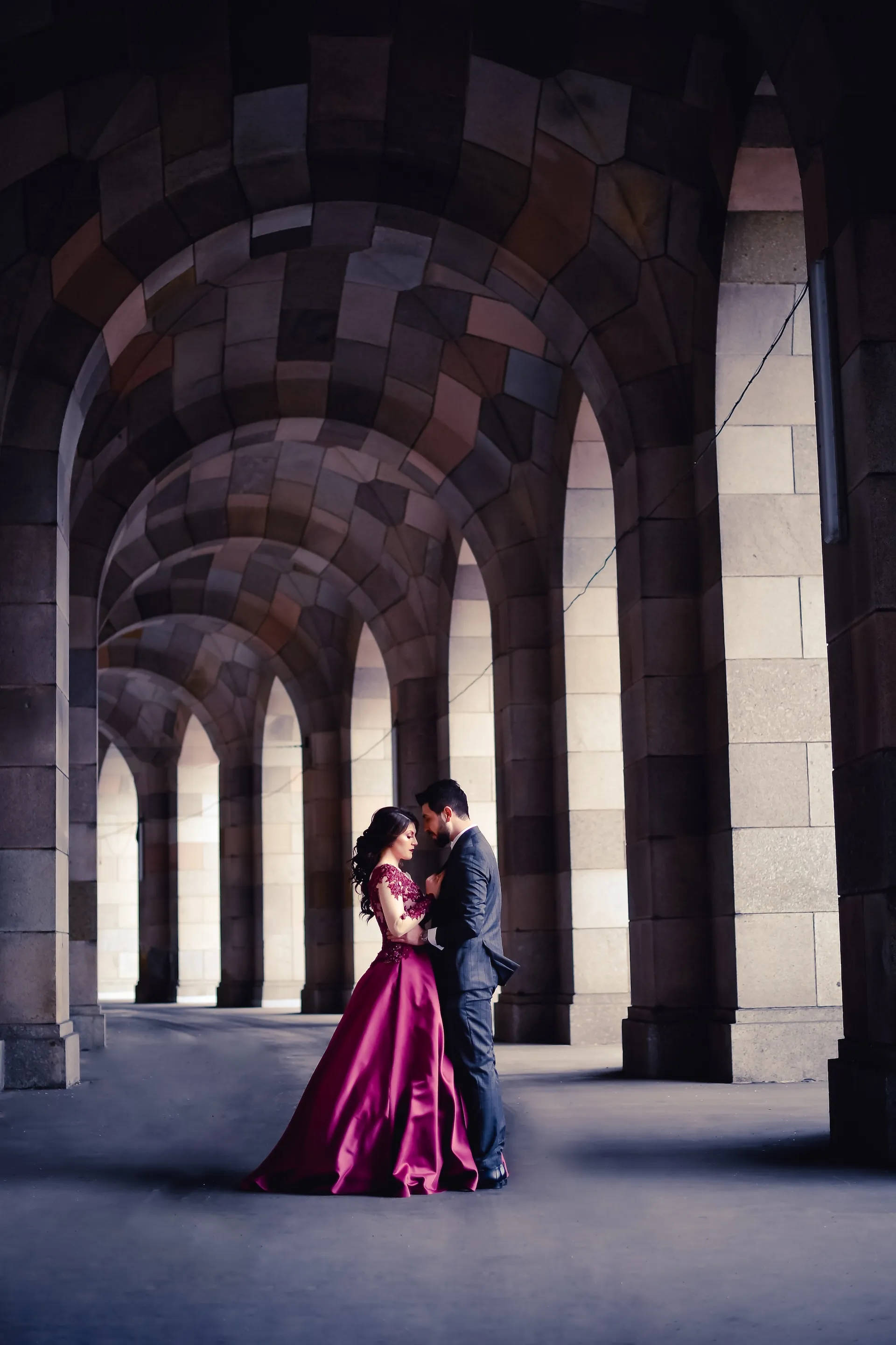 Brautpaar weinrotes Kleid im Steinbogengang